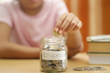 Hand's girl holding coins putting in glass with books on the table.saving for education concept.