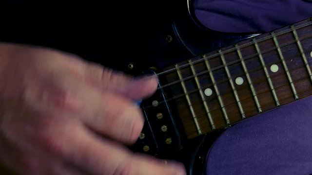 Strumming hand closeup on black electric guitar