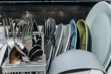 open dishwasher close up clogged with clean washed dishes. dry cutlery closeup. spoons forks. mugs,...