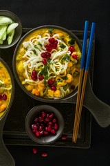 laks with pumpkin and coconut milk, rice noodles, broccoli and pomegranate seeds in portioned black plates onlaksa with pumpkin and coconut milk, rice noodles, broccoli and pomegranate seeds 