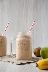 Smoothie with bananas, kiwi, apples and chia seeds in glass jars, side view. Closeup.