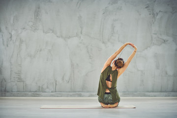 Obraz premium Woman sitting in on the mat in Side Mountain Pose. Backs turned.