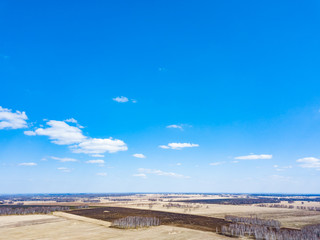 Fototapeta premium Panorama from the air on the lush meadows and fields with colorful plots of agricultural crops before sowing in spring outside the city in the sun under a blue sky and white clouds. Nature in season.