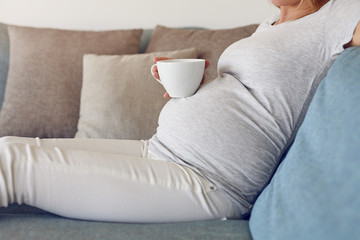 Bauch einer schwangeren Frau mit einem Becher Tee - obrazy, fototapety, plakaty