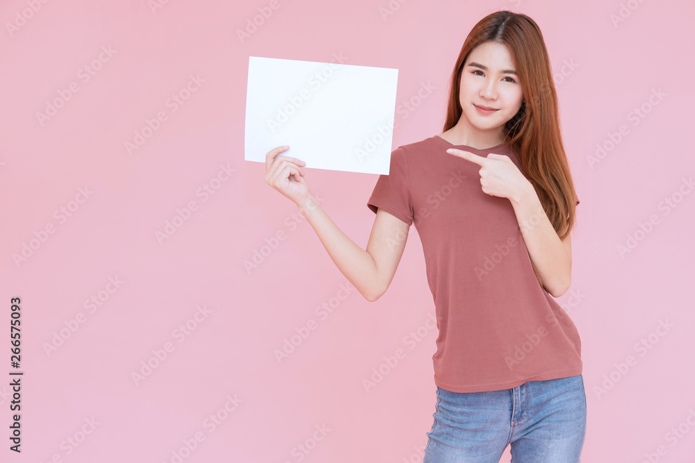 Wall mural young asia smiling woman holding advertising sign board and pointing finger. isolated portrait on pi