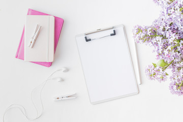 Flat lay blogger or freelancer workspace with a mockup clipboard and branches of lilac on a light background