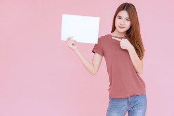 young asia smiling woman holding advertising sign board and pointing finger. Isolated portrait on pink background with copy space