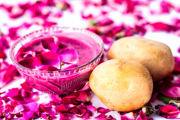 Best face mask or face pack to reduce blemishes and dark patches isolated on white i.e. Rose petals well mixed with potato juice in a bowl and raw potato and rose petals present on the surface.