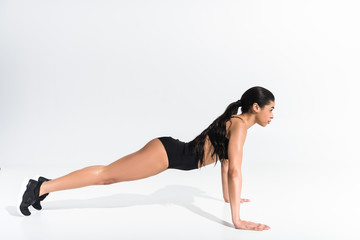 Fototapeta na wymiar side view of sportive african american girl doing push ups on white background