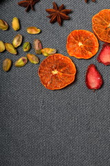 Fototapeta na wymiar Dried tangerines and strawberries, cut into pieces to decorate the dessert. Nearby are pistachios and anise. On a gray background.