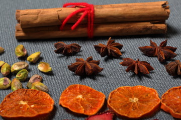 Dried tangerines and strawberries, cut into pieces to decorate the dessert. Nearby are pistachios, anise and cinnamon sticks tied with red thread. On a gray background.