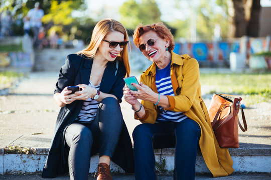 Mother and daughter in the park sharing content on their smartphones