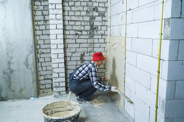 builder sitting on his hunkers plastering on block wall