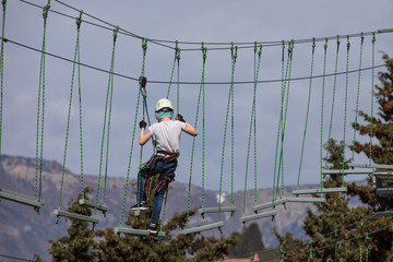 Boy climbing in a rope park against the sky, mountains and pine forest