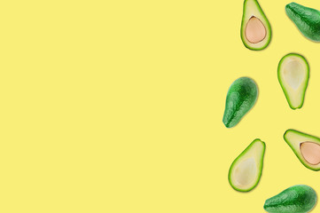 Scattered whole and halves of organic avocado with and without kernels on yellow table in kitchen or market. Top view. Cooking concept. Copy space for your text