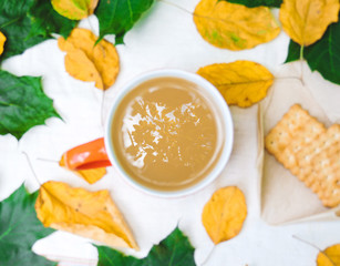 Cup of coffee, dry cracker cookies and dry leaves on an orange background. Autumn background, flat lay. Autumn composition. Autumn mood, top view. Cup of autumn coffee and yellow dry leaves.