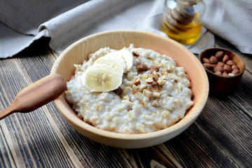 Oatmeal porridge with bananas, nuts and honey in a wooden bowl 
