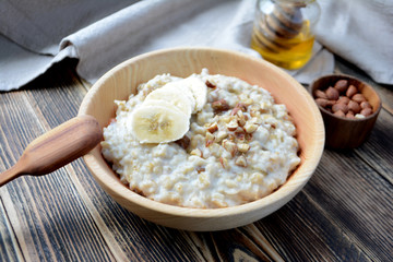 Oatmeal porridge with bananas, nuts and honey in a wooden bowl 