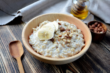 Oatmeal porridge with bananas, nuts and honey in a wooden bowl 