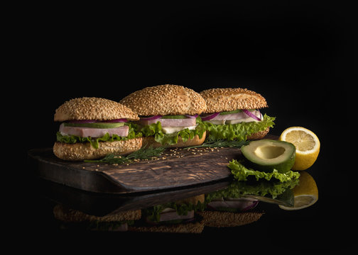  Sandwiches with ham, avocado, cheese and greens on a dark background