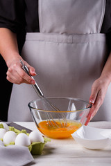 young woman in a gray aprons breaks the eggs