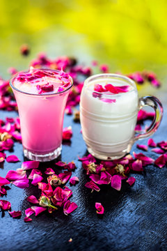 Popular Indian & Asian Summer drink on wooden surface i.e. Gulab falooda or gulab ka sherbat with some rose petals on black colored shiny surface.