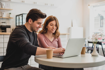 Two young people working with a laptop in a cafe and drinking coffee