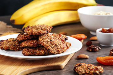 oat cookies chips and ingredients banana walnuts almonds raisin dried apricots on wooden table soft focus close up
