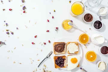 top view of plate with toasts, jam and fried egg near glasses of water and orange juice on white