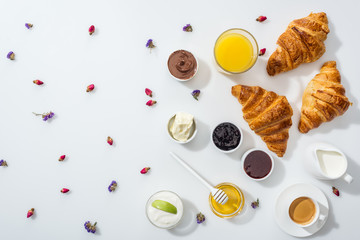 top view of tasty croissants near bowls with jam, orange juice and dried flowers on white