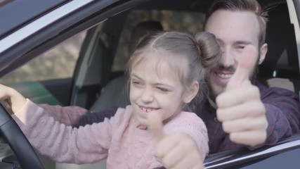 Portrait of hipster father and pretty daughter sitting on driver's seat and happily with smiles thumbs up