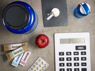 big blue protein jar, raw protein bars, red apple and calculator