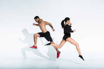 Fototapeta na wymiar sportive african american girl and athletic mixed race man running on white background
