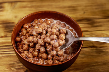 Cereal chocolate balls with milk in a bowl on wooden table. Spoon with breakfast