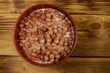 Cereal chocolate balls with milk in a bowl on wooden table. Top view