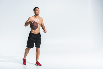 handsome athletic mixed race man in black shorts and red sneakers playing ball on white
