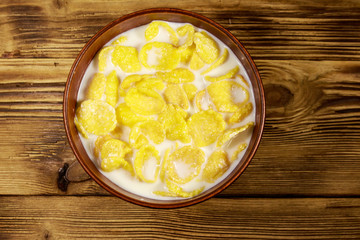 Cornflakes with milk in a bowl on wooden table. Top view