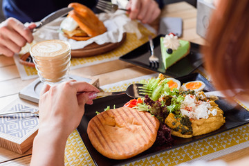 Girl eating delicious breakfast with boiled eggs, pumpkin puree, lettuce, cheese and fresh bread on a black plate on a yellow set on a wooden table in a restaurant.  Close up