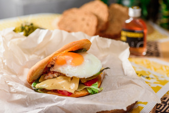 Burger with fried egg, chicken, cheese, tomatoes and other vegetables on a craft paper on yellow background in a restaurant. Series of photos for the menu.