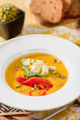 Pumpkin cream soup with cheese Dor Blue, bell pepper, pumpkin seeds in a white plate on yellow set on a wooden  table in a restaurant. close-up. top view. flat lay