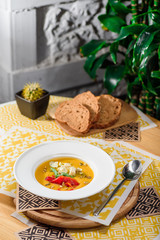 Pumpkin cream soup with cheese Dor Blue, bell pepper, pumpkin seeds in a white plate on yellow set on a wooden  table in a restaurant. close-up. top view. flat lay