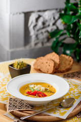 Pumpkin cream soup with cheese Dor Blue, bell pepper, pumpkin seeds in a white plate on yellow set on a wooden  table in a restaurant. close-up. top view. flat lay