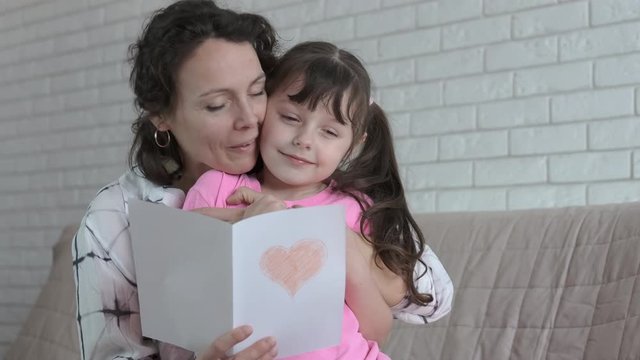The child gives mom a valentine. Daughter gives mother a card with a heart.