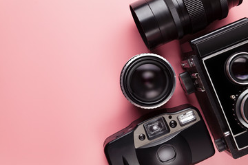 Old analog cameras and lenses on a pink table background