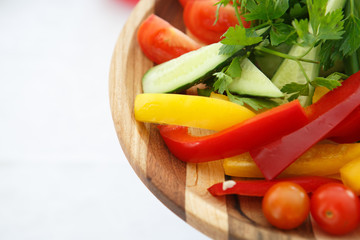 Organic farm. Fresh vegetables in wooden plate: yellow and red bell pepper, onion, tomato and cucumbers.