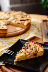 Piece of pumpkin pie with figs, blue cheese and pumpkin seeds on a black plate close up on the background of a whole round pie. Close up