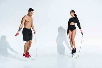 athletic mixed race man and sportive african american woman jumping with skipping ropes on white - Powered by Adobe
