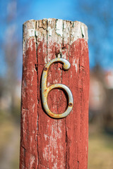 Rusty number six on a red wooden pole at the entrance of an house