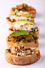 Variety of canape with hummus, tomato, avocado, cheese, walnut and fresh vegetables on white background. Top view of healthy snack concept.