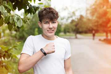 Naklejka na ściany i meble An adolescent boy after an outdoor exercise, jogging looks at a fitness bracelet on his arm and rejoices at a lot of mileage